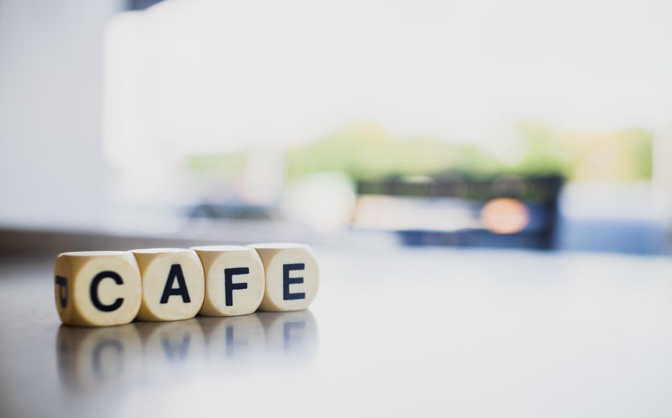 Close-up of wooden dice spelling cafe on a reflective surface with a blurred background. Bright and inviting.