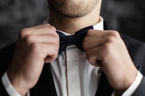 Free Close-up of a groom adjusting his bow tie, showcasing elegance and readiness on a special day. Stock Photo