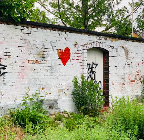 Free Photograph of a graffitied brick wall featuring a red heart and greenery. Stock Photo