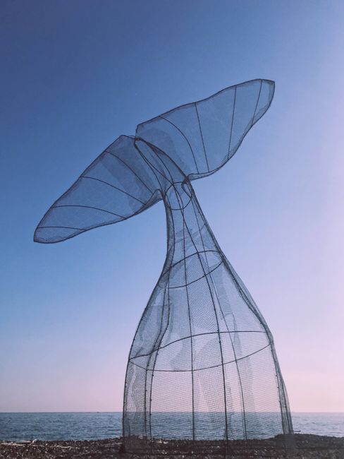 A breathtaking metal whale tail sculpture against a clear blue sky by the Ligurian Sea in La Spezia, Italy.