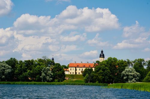 Free Scenic view of Niasviž Castle surrounded by trees and lake in Belarus under a vibrant blue sky. Stock Photo
