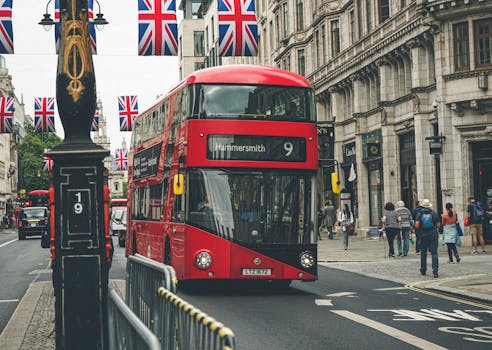 Iconic red double-decker bus on a busy street in London, England, with British flags overhead.