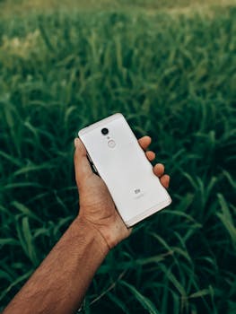 Close-up of hand holding a smartphone against lush greenery in India, outdoors.