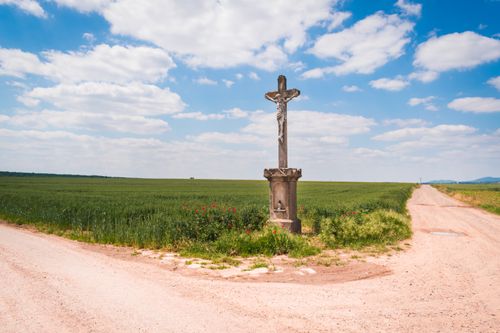 Free A solitary cross at a rural crossroads under a blue sky with white clouds. Stock Photo