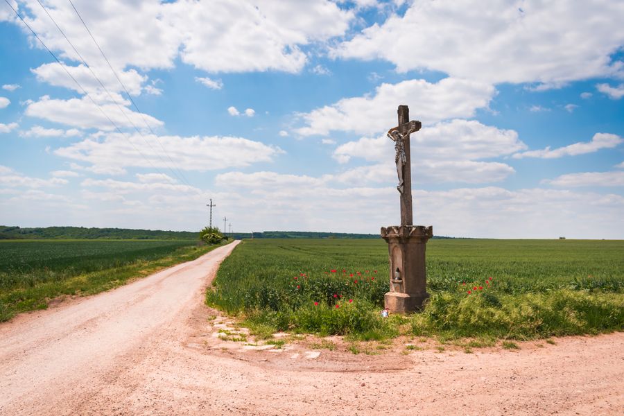 Picturesque rural scene featuring a cross by a dirt road under a vibrant sky.