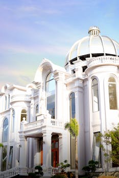 Luxurious white mansion featuring a striking dome and classic architectural elements under a bright sky.