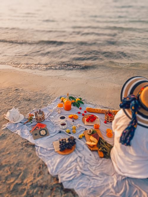Free Elegant beach picnic setup with fruits and drinks by the sea at sunset. Perfect for relaxation and enjoyment. Stock Photo
