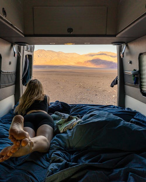 Woman Lying in a Campervan with Opened Doors and Looking at a Desert Landscape 