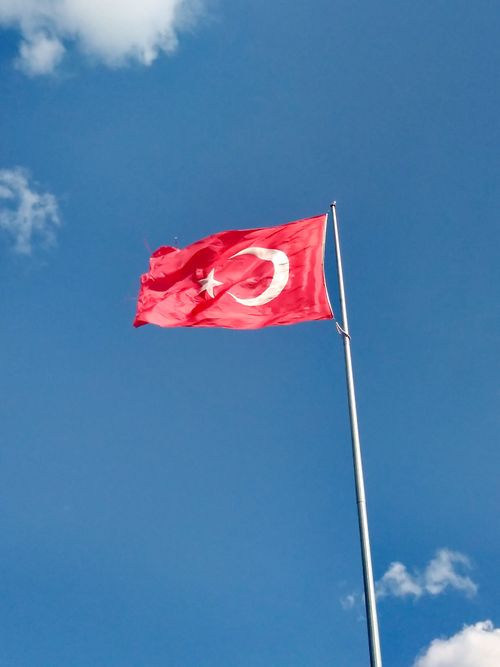 Free National Turkish flag waving on a pole against a bright blue sky with clouds. Stock Photo