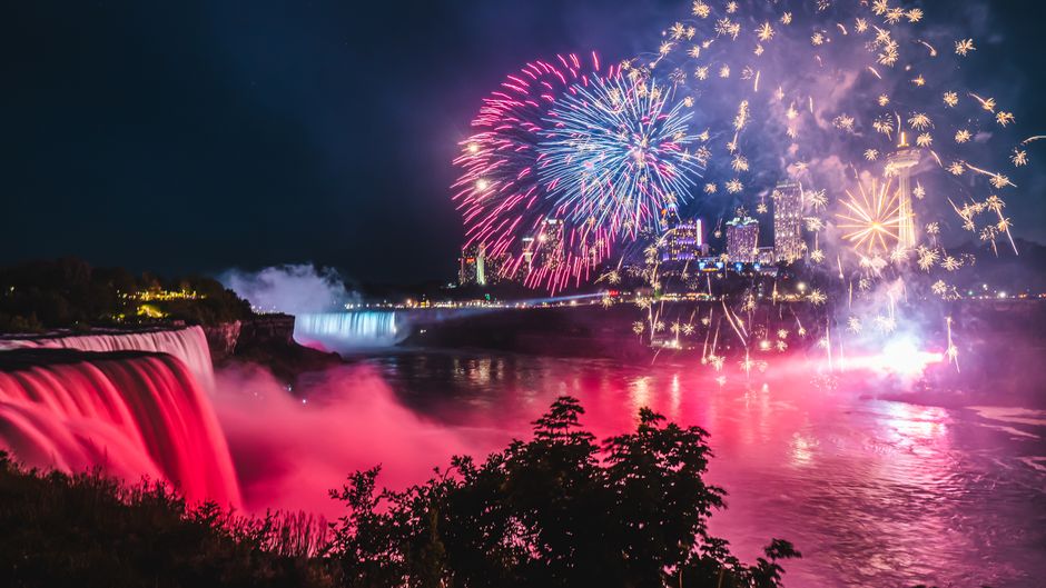 Niagara Falls Canada Tour: Helicopter, Boat Cruise & Journey - A vibrant fireworks display illuminates the night sky over Niagara Falls, showcasing the stunning waterfalls and city lights.