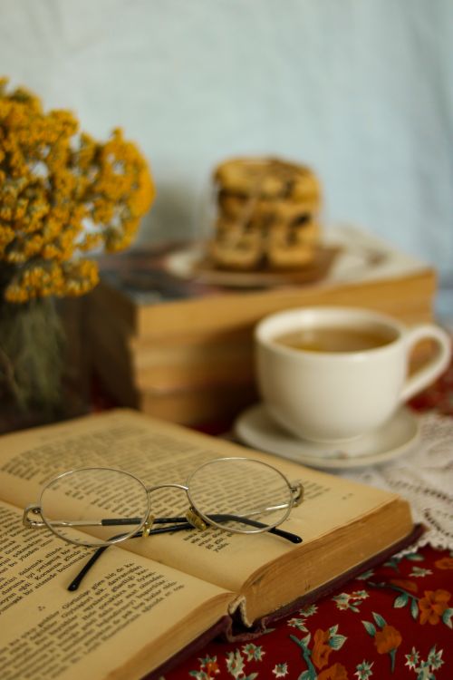 Free Warm still life setting with tea, book, glasses, and flowers for a cozy reading moment. Stock Photo