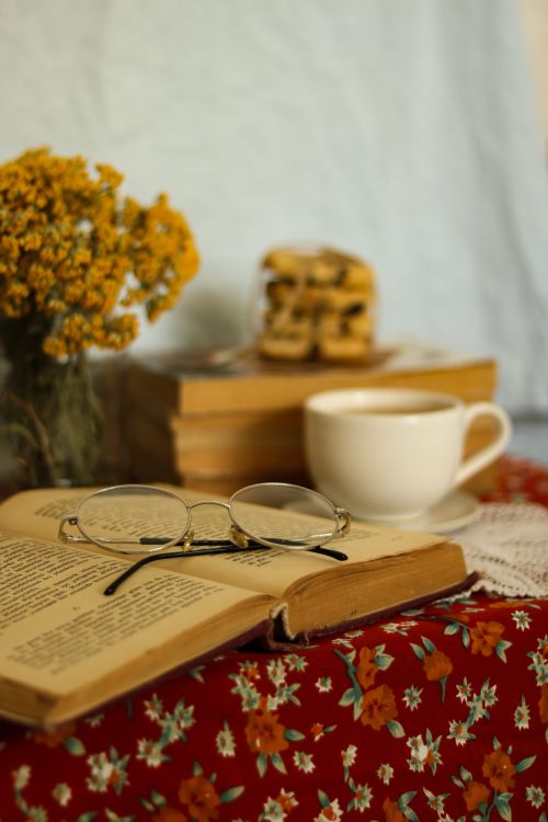 Free A warm, inviting reading setup featuring books, flowers, and a cup of coffee on a floral tablecloth. Stock Photo