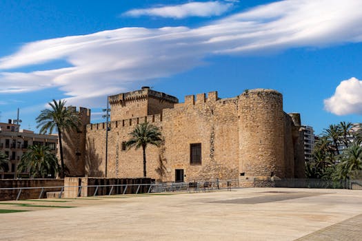 Beautiful view of the historic Altamira Castle in Elche with palm trees under a clear blue sky.
