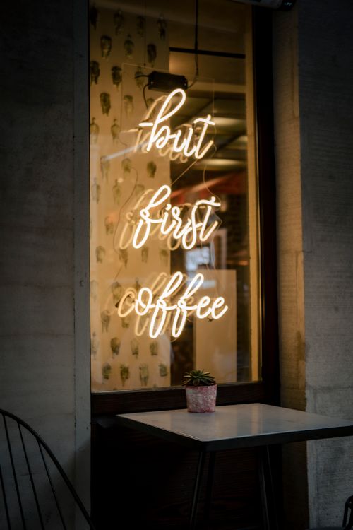 Free Illuminated neon sign saying 'but first coffee' on a café window. Stock Photo