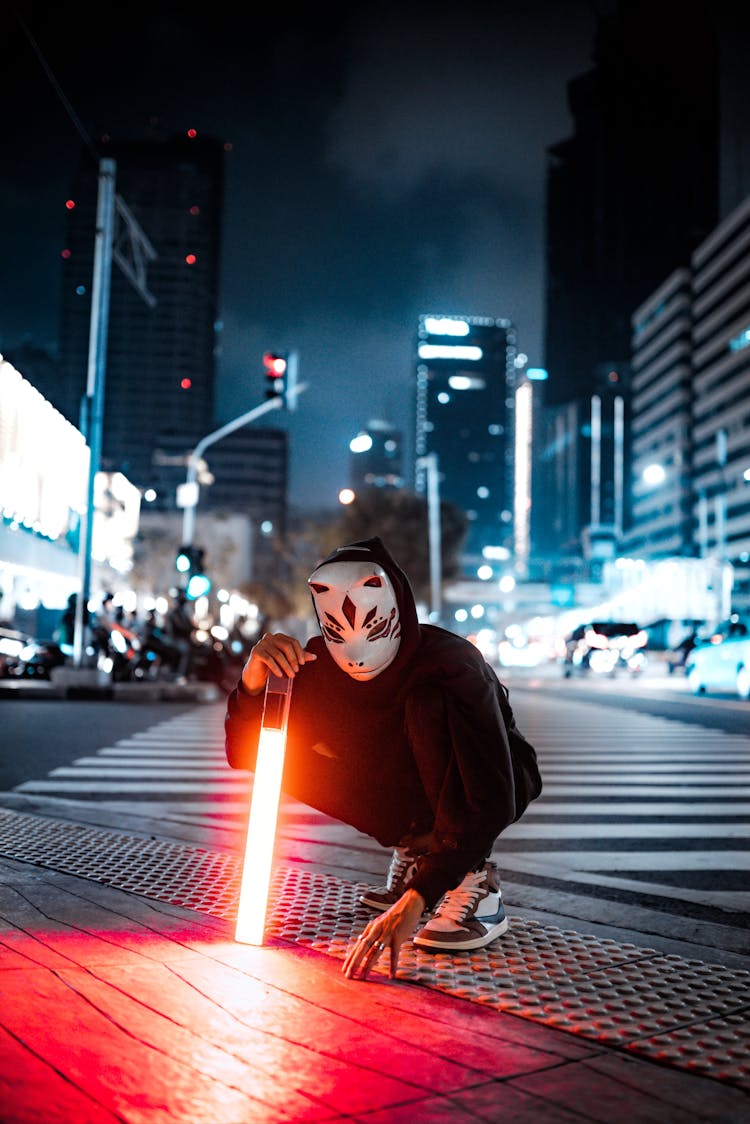 Masked Person With Light Saber On City Street At Night