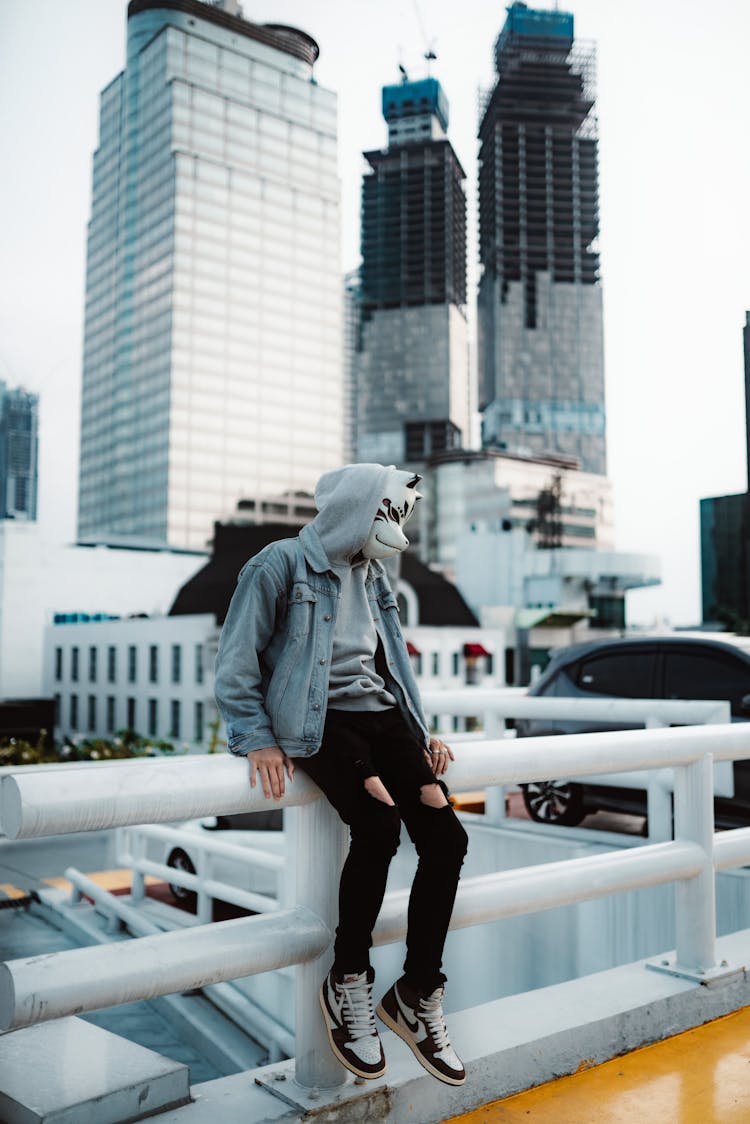 Masked Person With Sitting On Railing On City Street