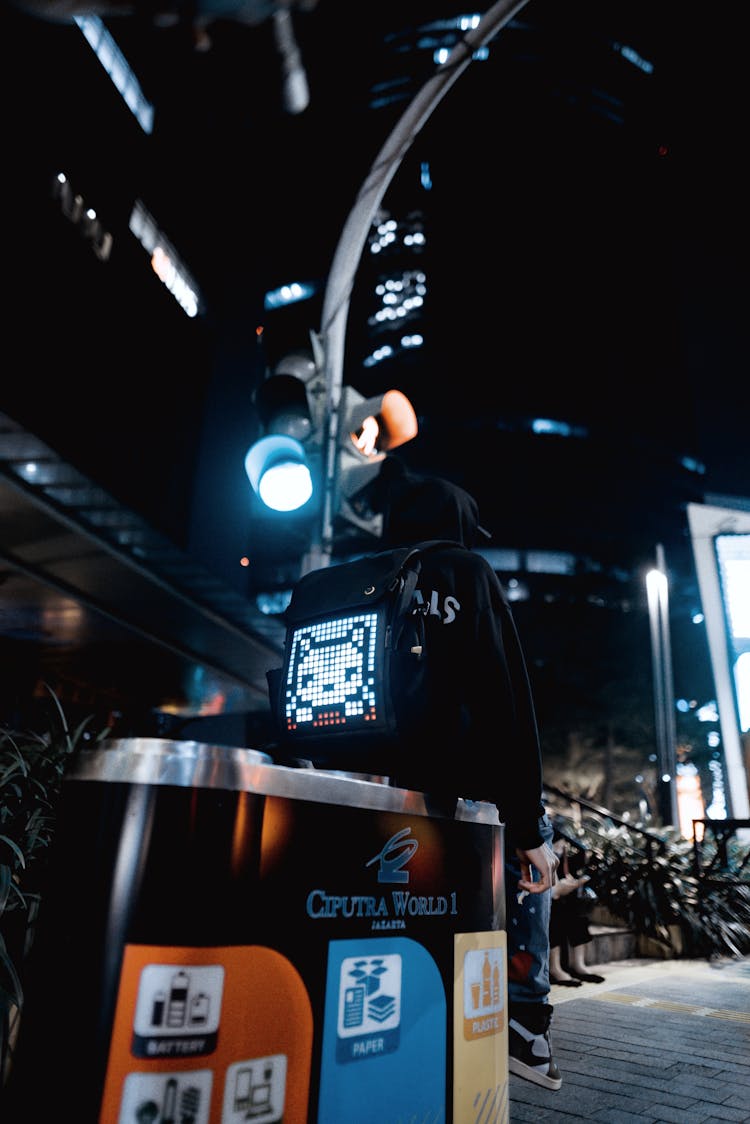 Person With Lit Up Backpack Sitting On Trashcan