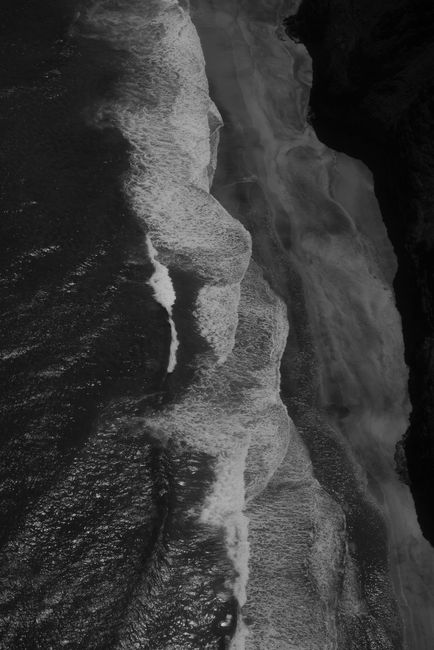 A striking black and white aerial shot of waves crashing on a rocky coastline, creating a dramatic effect.