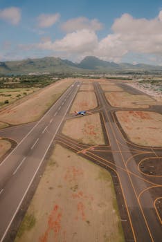 Aerial shot of an airport runway featuring an airplane, set against mountainous landscape.