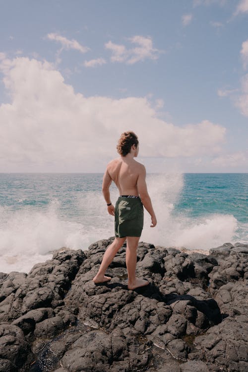 Shirtless Man Standing on Rocky Coast