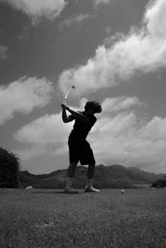 Silhouette of a golfer swinging a club on a picturesque course.