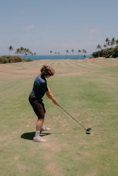 Photo by Juan Gomez A golfer in mid-swing on a beautiful coastal golf course with a clear sky and ocean view.