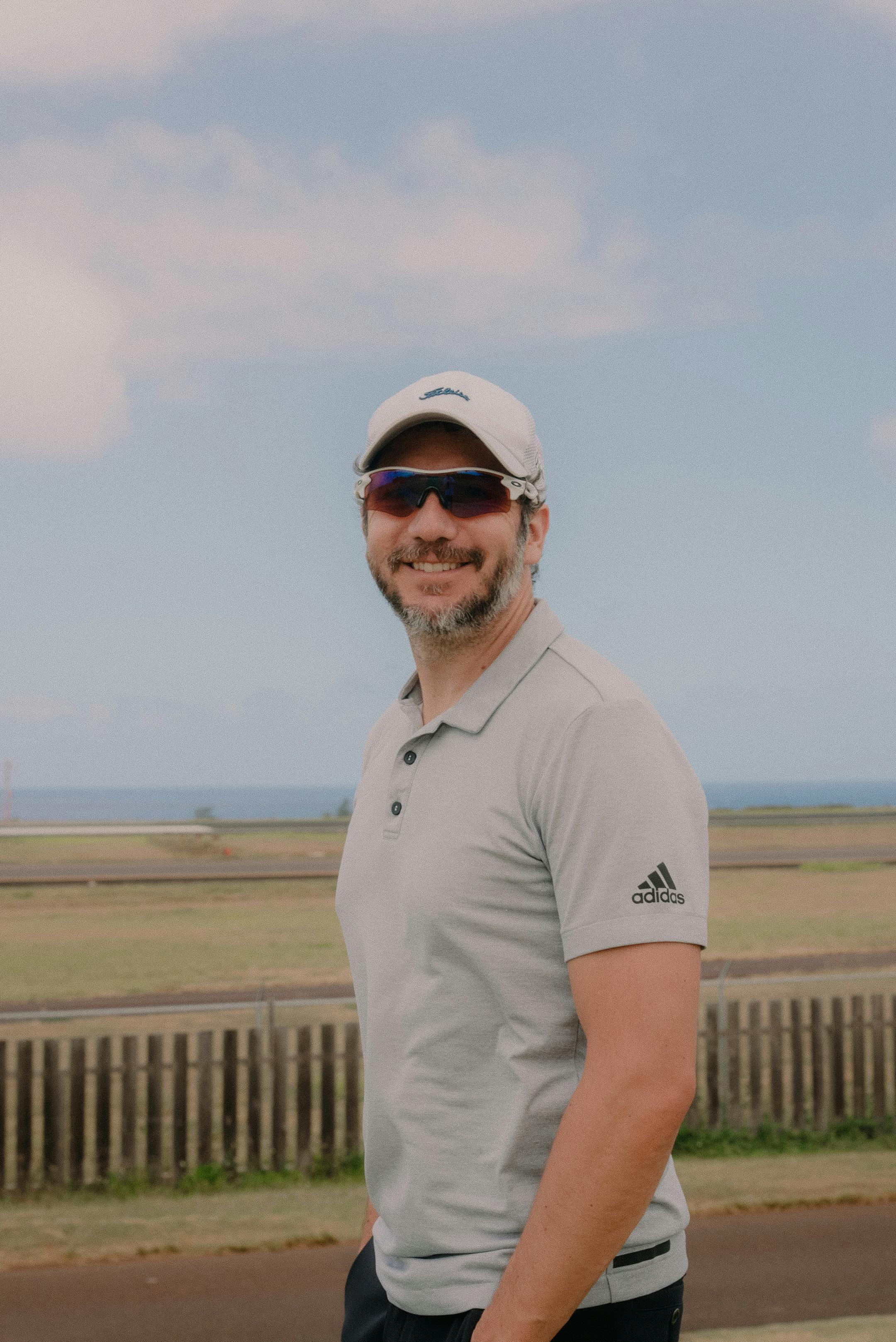 Smiling man in sportswear enjoying a sunny day outdoors with clear sky and ocean backdrop.