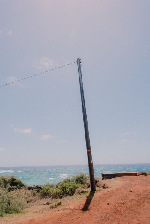Free A solitary telephone pole stands by the ocean against a clear blue sky, surrounded by natural beauty. Stock Photo