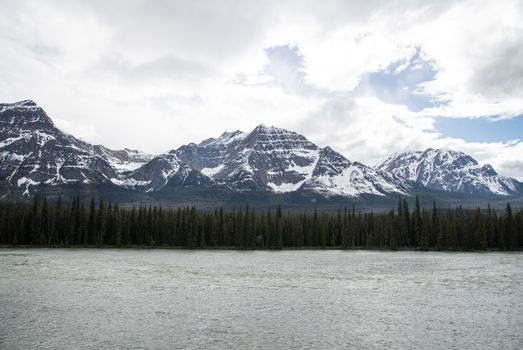 Breathtaking view of snow-capped mountains, forest, and lake in Alberta, Canada.