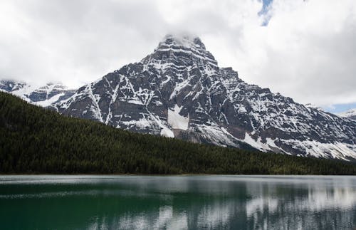 Lake Near Snow Covered Mountain Under Cloudy Sky