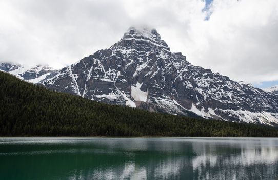 Dramatic snowy mountain peaks reflected in a serene lake surrounded by evergreen forests.
