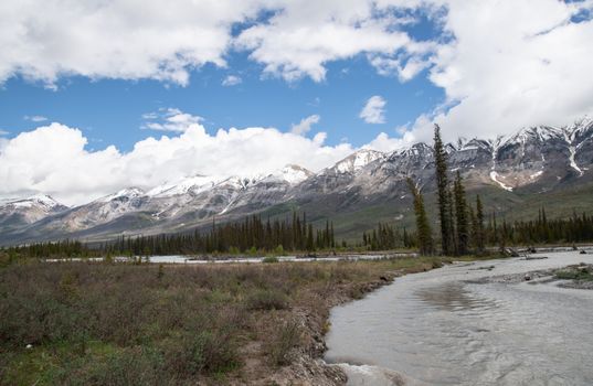Scenic view of snowcapped mountains with a winding river and forested landscape under a blue sky.
