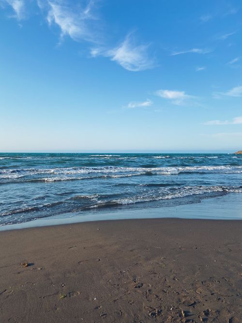 Free Tranquil beach scene with gentle waves under a bright blue sky, perfect for serene relaxation. Stock Photo