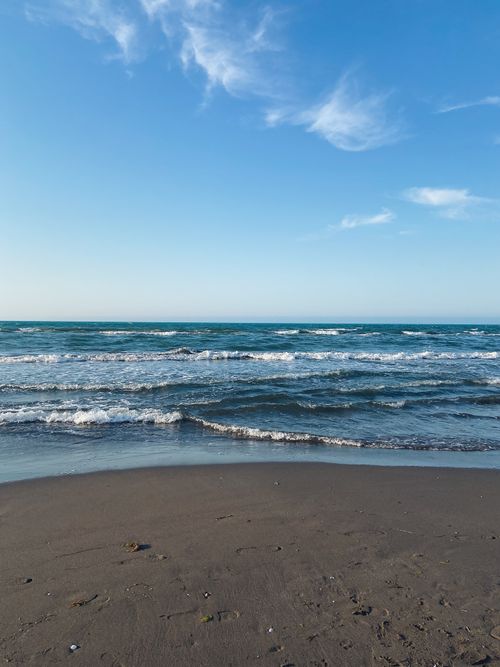 Free Peaceful view of gentle ocean waves lapping against a sandy beach under a clear blue sky. Stock Photo
