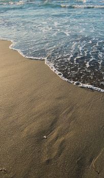 Calm ocean waves meet golden sandy beach at sunset, creating a tranquil coastal scene.
