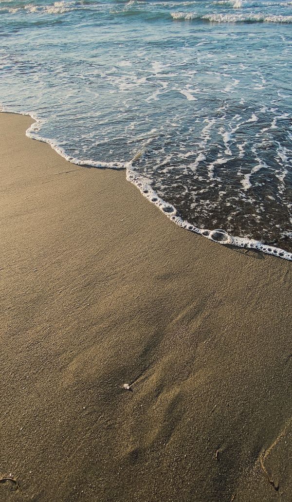 Ondas calmas do oceano encontram a praia de areia dourada ao pôr do sol, criando uma cena costeira tranquila.