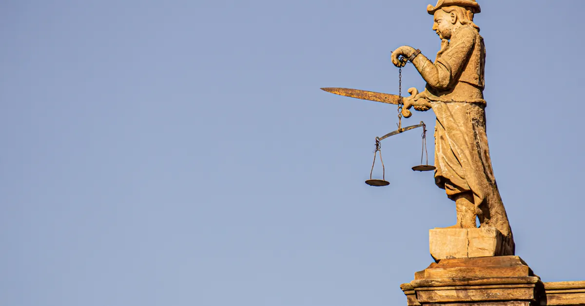 A Lady Justice statue with a sword and scales against a clear sky