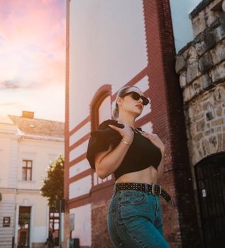 Stylish woman in crop top and jeans poses in Cluj-Napoca, Romania, during sunset.