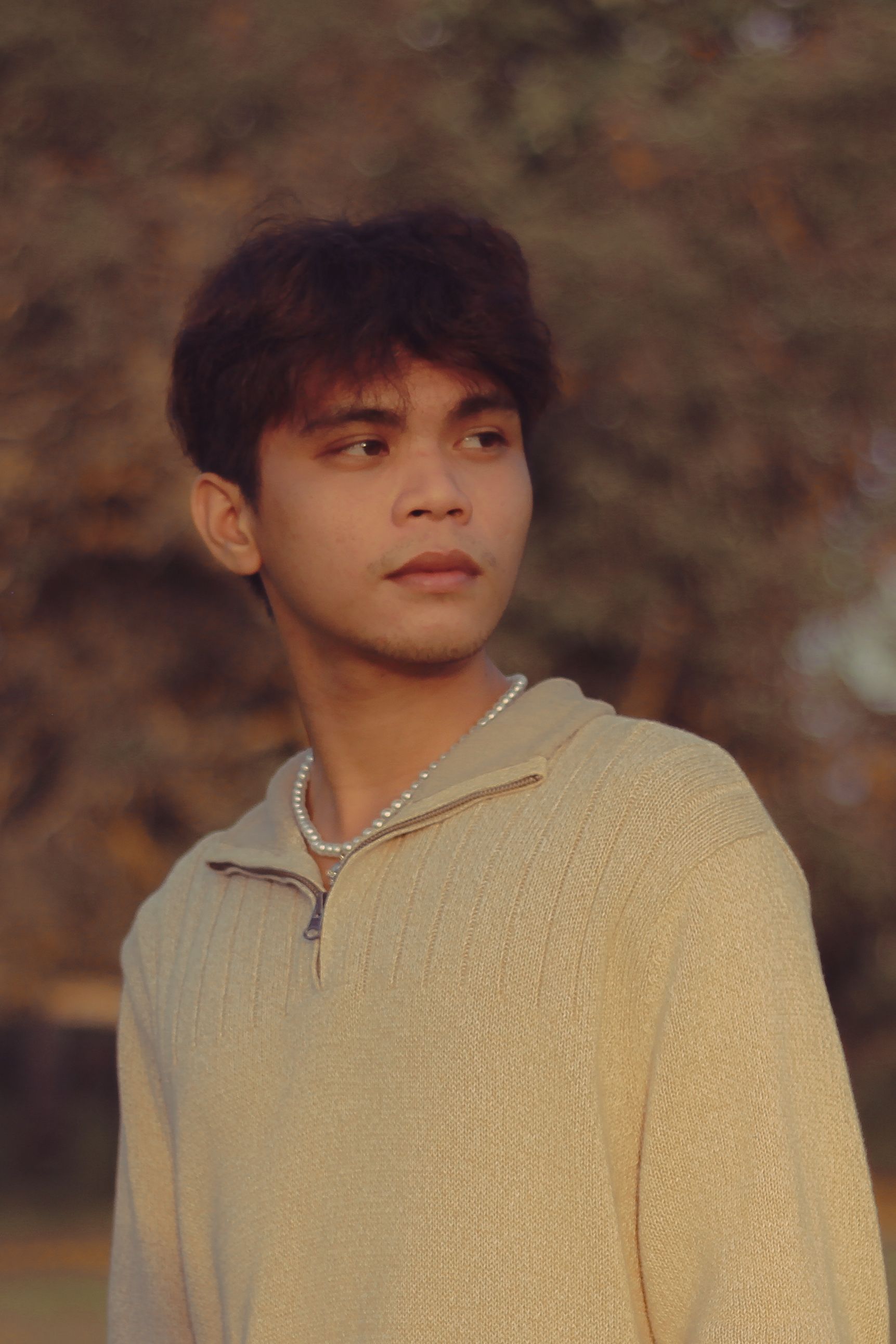 Warm-toned portrait of a young man looking over his shoulder in an outdoor autumn setting.