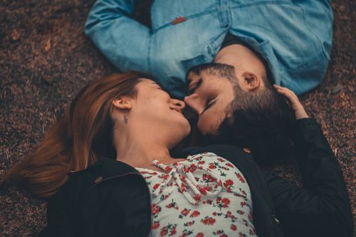 Free A loving couple lies on grass, sharing an intimate moment outdoors. Stock Photo
