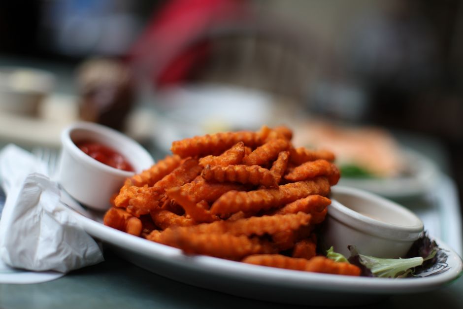 Crinkle-cut sweet potato fries served with ketchup on a white plate, ideal for food lovers.