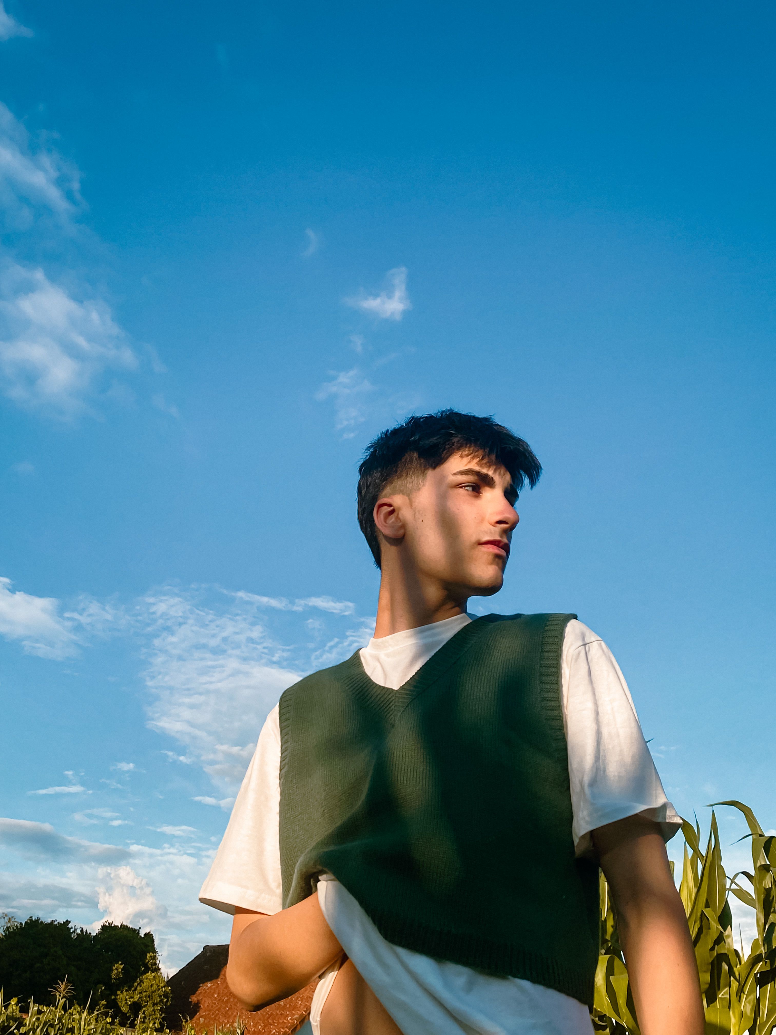 Portrait of a young man outdoors in a green vest against a blue sky.