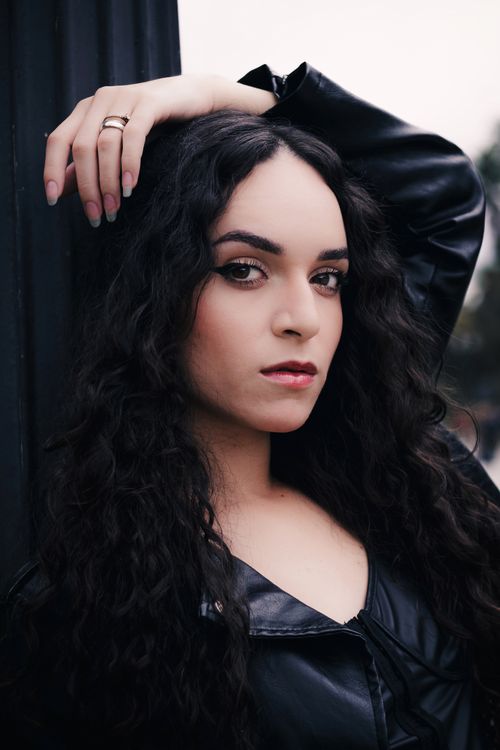Free A captivating portrait of a confident woman with curly hair in a leather jacket. Outdoors with a serious expression. Stock Photo