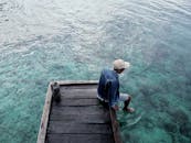 一个人坐在木制码头上，将脚浸入清澈的水中，尽显悠闲与放松