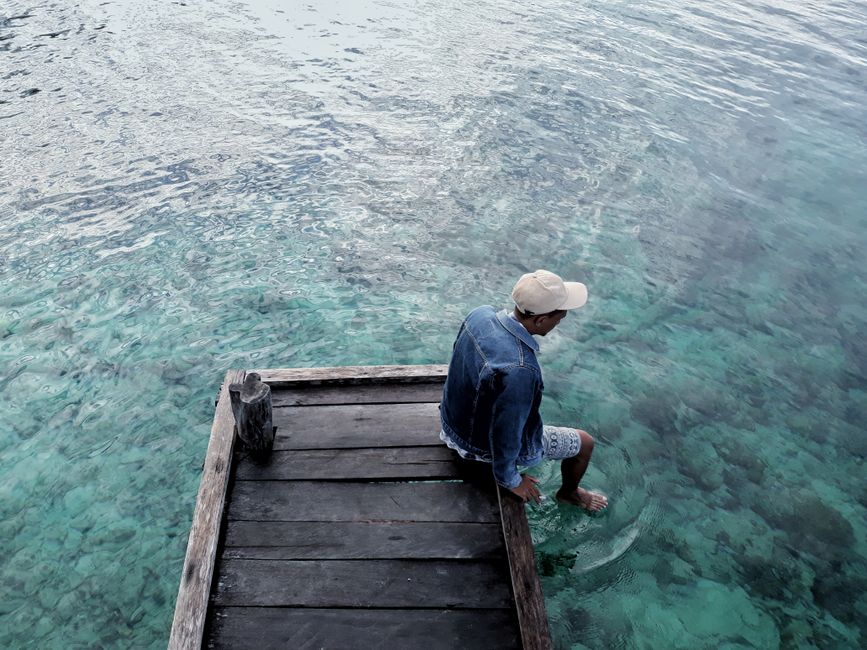 A man sits on a wooden dock, dipping his feet into crystal clear water. Perfect for leisure and relaxation themes.
