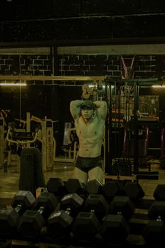 A shirtless man showcasing his muscles and fitness in a well-equipped gym.