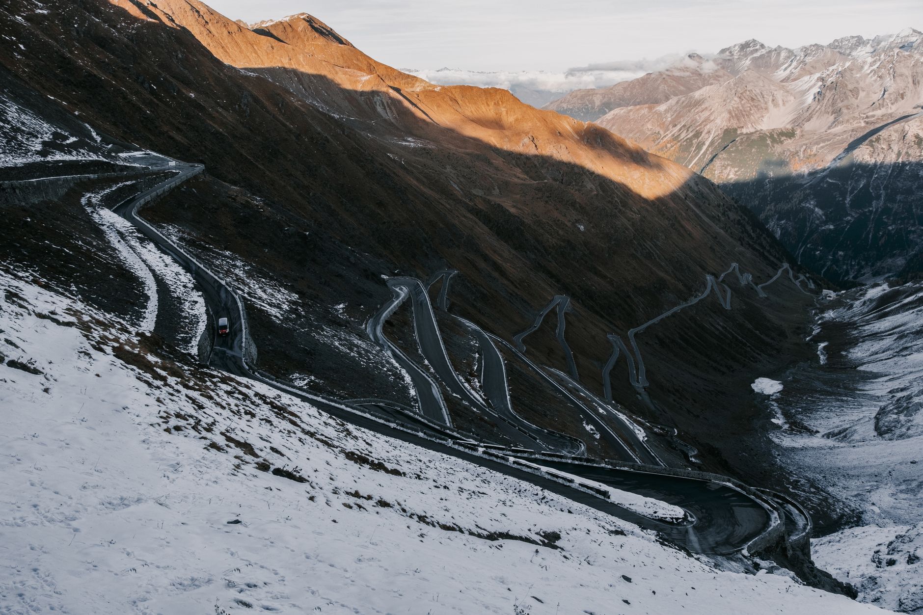 Vehicle driving a high-altitude mountain pass with hairpin switchbacks at golden hour