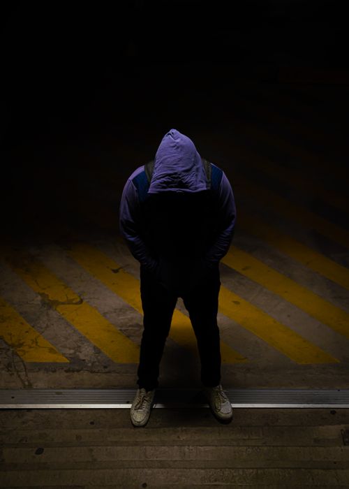 Free A person in a hoodie stands under a spotlight casting a dramatic shadow in a dark environment. Stock Photo