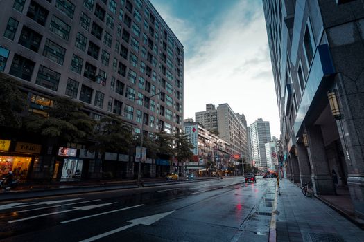 Urban street scene with high-rise buildings reflecting on wet roads after rain.