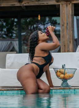 Woman in swimwear enjoying grapes by the poolside, embodying summer vibes.